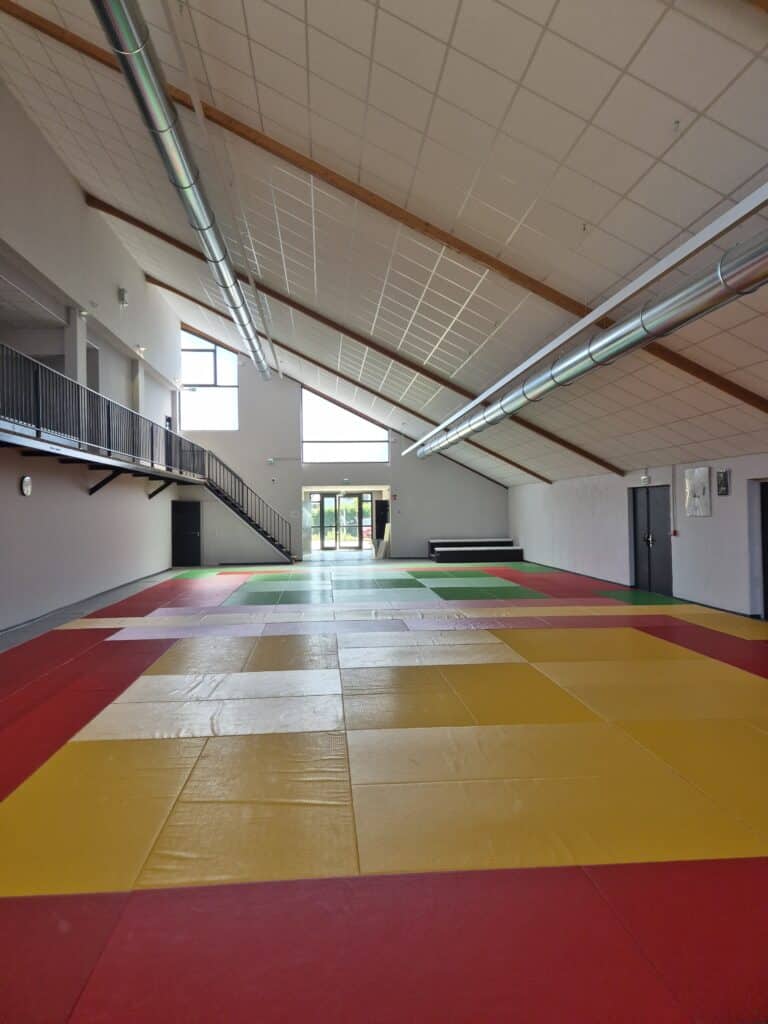 Dojo, Tatami : salle de sport moderne et colorée Intérieur de gymnase moderne. Tapis tatami rouges, jaunes et verts couvrent le sol. Plafond incliné avec poutres et conduits de ventilation métalliques.